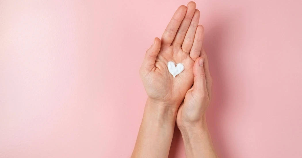 A pair of hands gently cupped together with heart-shaped skincare cream